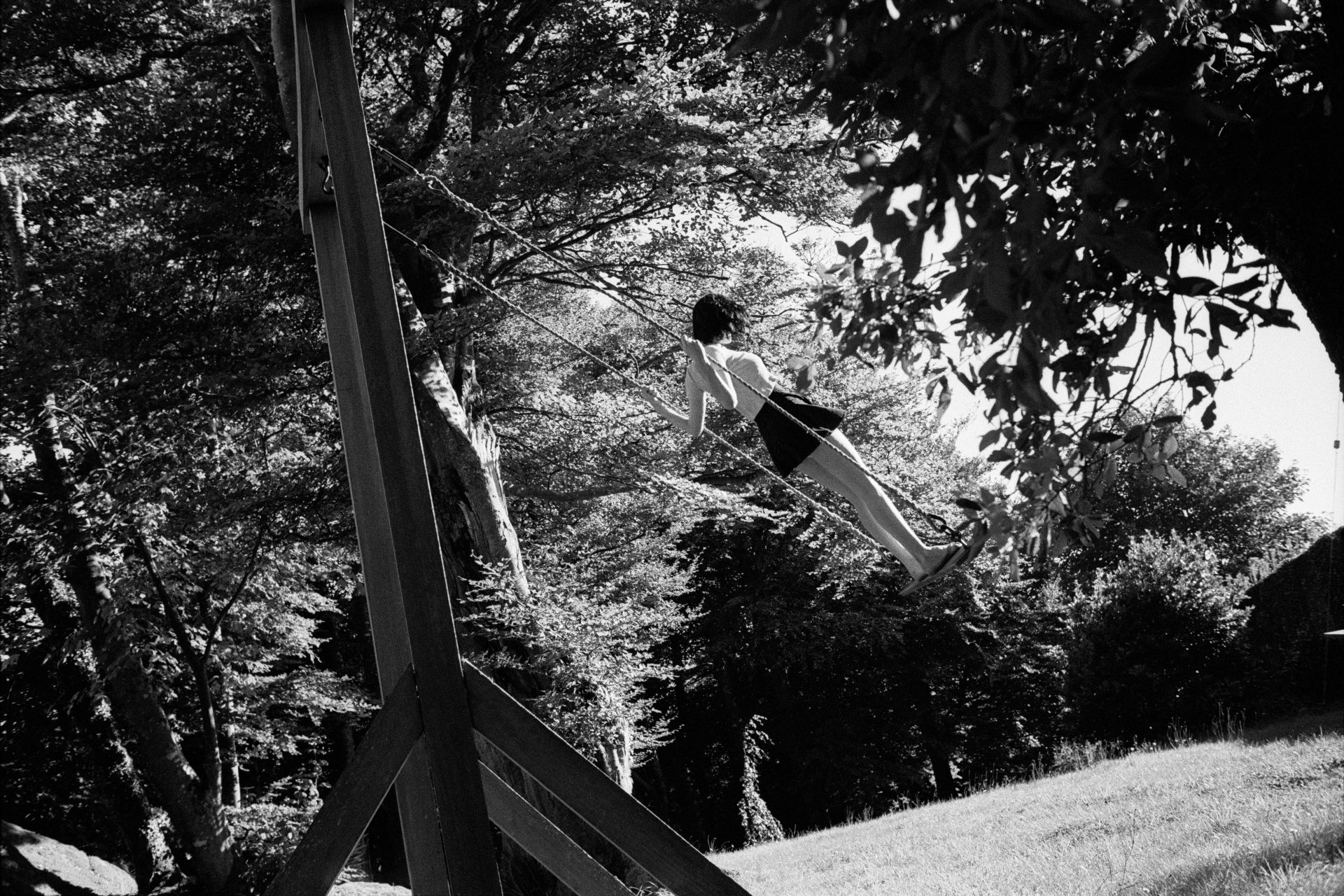 Susie standing barefoot on a swing in the air, surrounded by trees