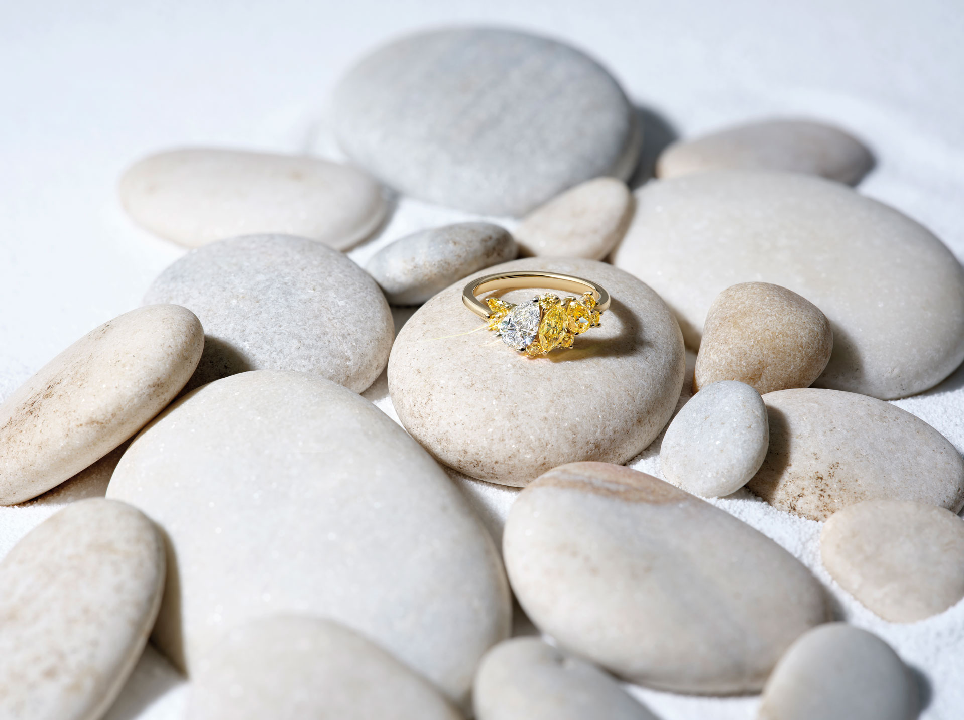 A yellow diamond ring on smooth, round pebbles